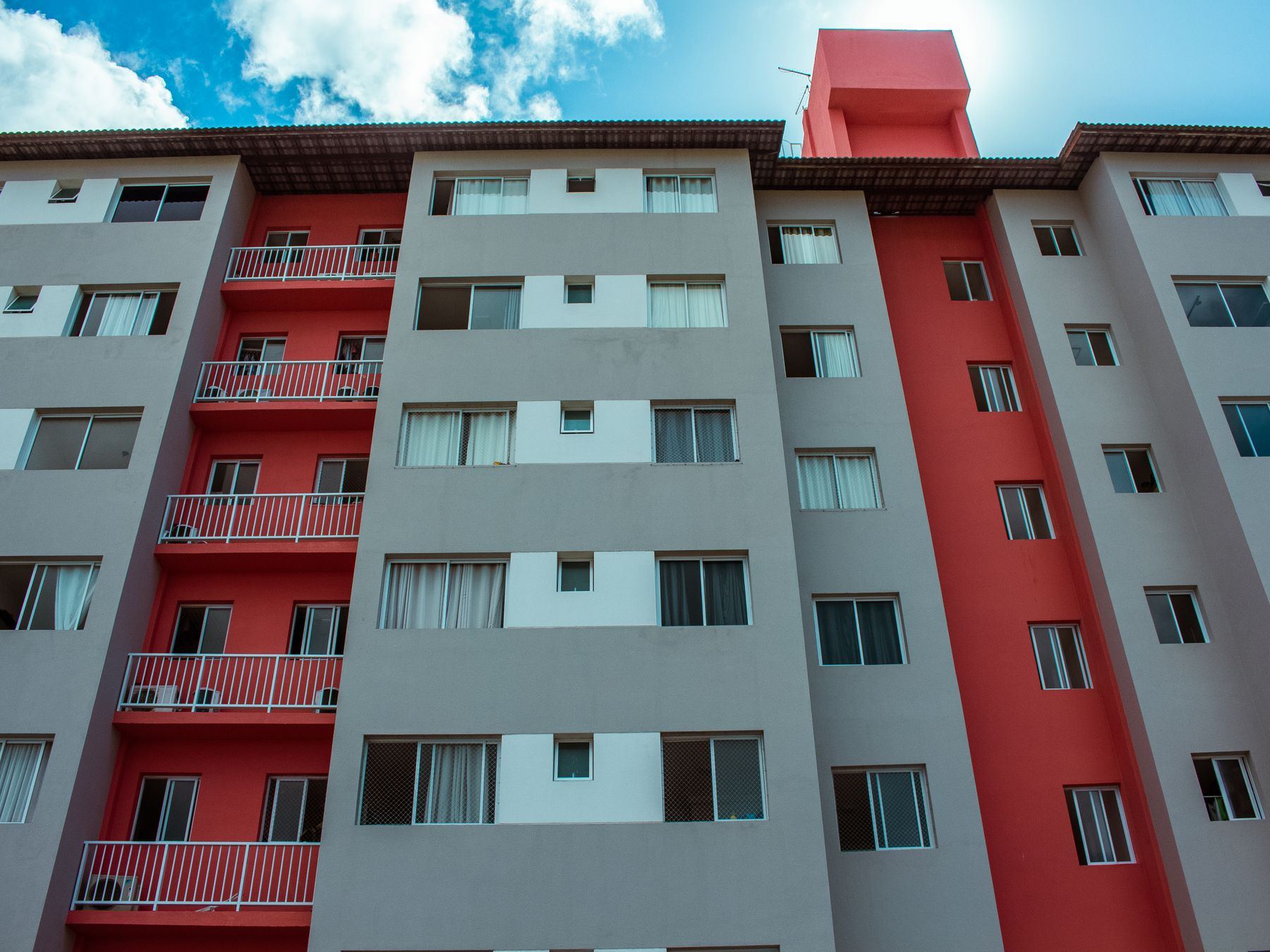 A high-rise residential building featuring a striking red facade and balconies against a blue sky.