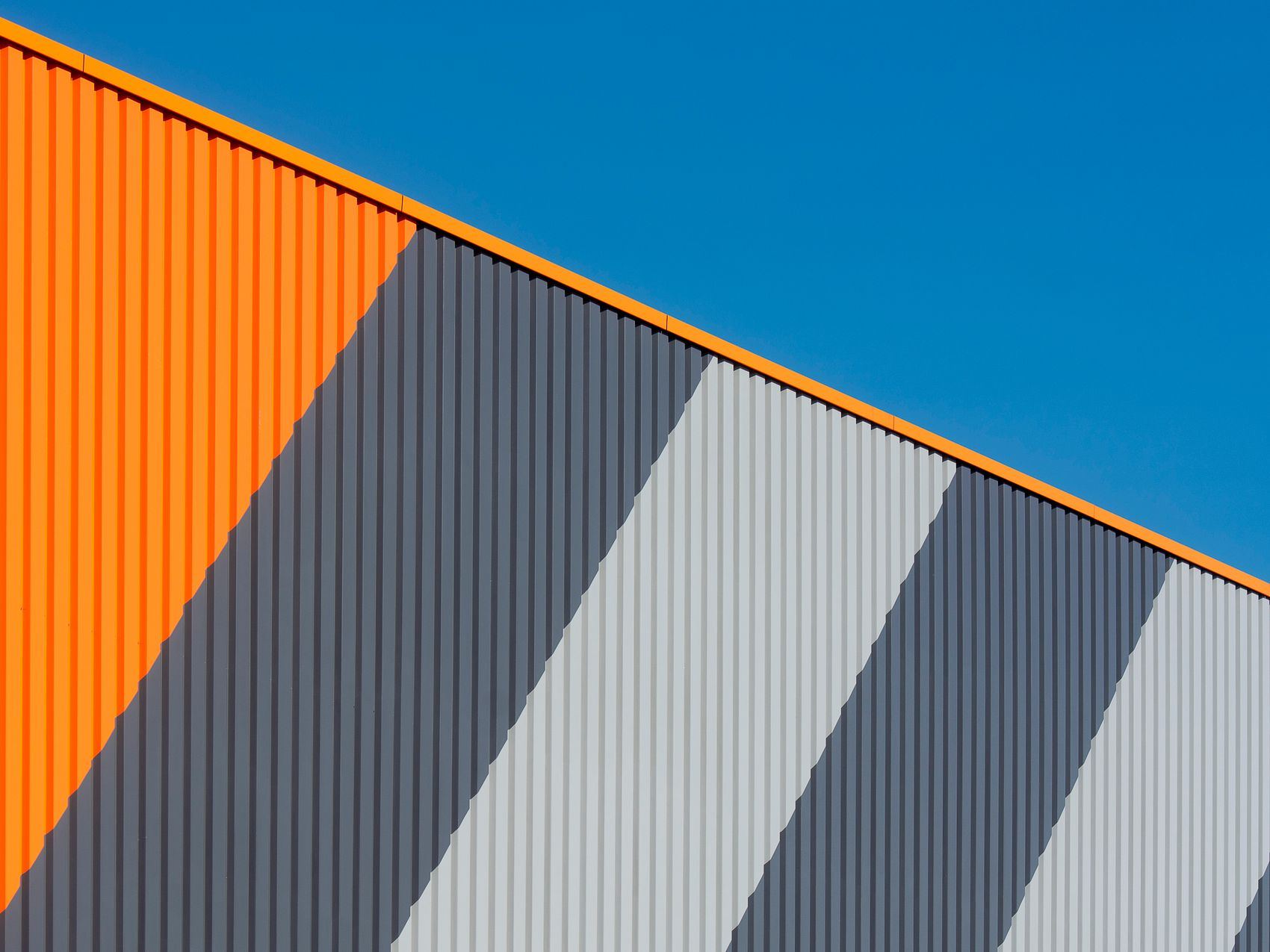 Abstract view of a modern industrial facade with orange and gray stripes under a clear blue sky.